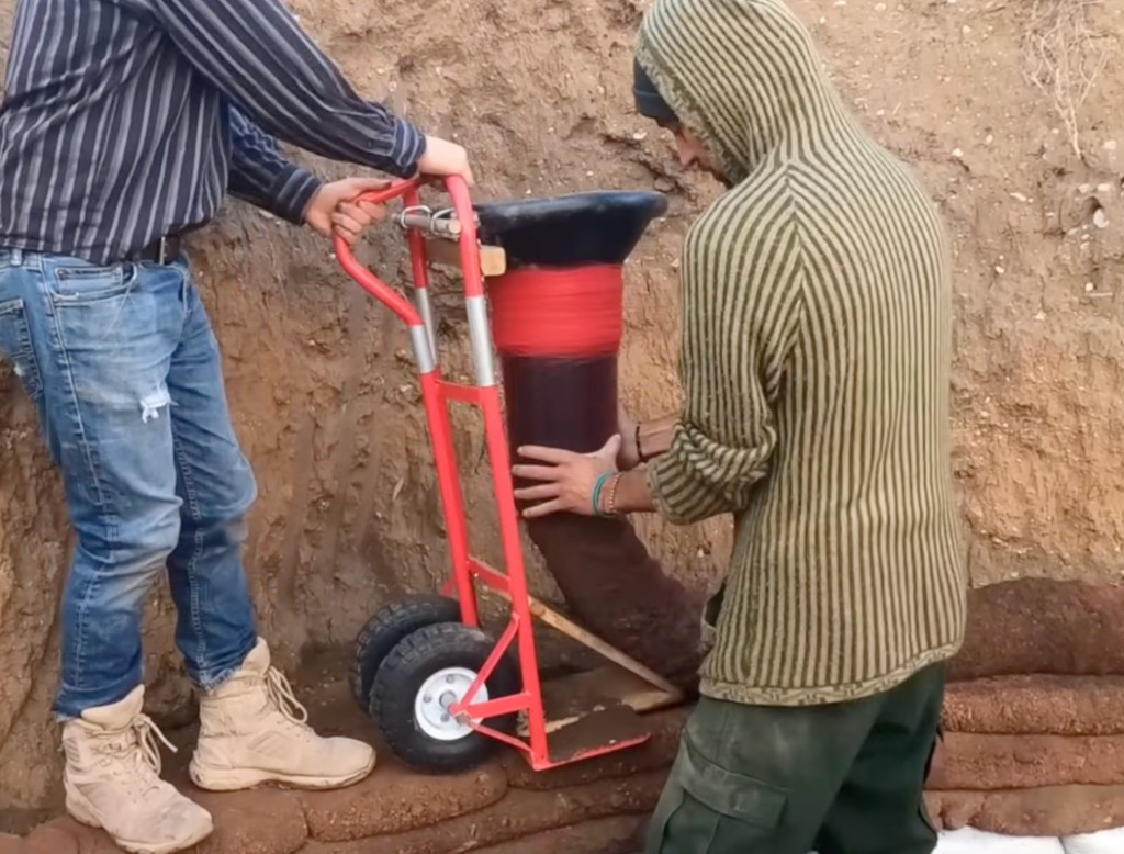 Two builders filling and laying a continuous mesh tube with Adobe Ninja on an earthbag wall